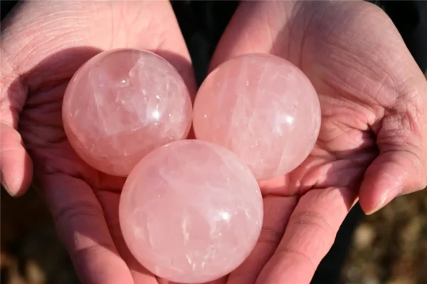 May include: Three polished rose quartz spheres with a translucent, pale pink appearance and natural internal inclusions. Each stone is spherical in shape, feat May include: Three polished rose quartz spheres with a translucent, pale pink appearance and natural internal inclusions. Each stone is spherical in shape, featuring a smooth, reflective surface that catches the light, showcasing the mineral's texture.