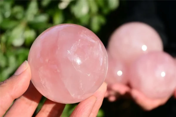 May include: A smooth, polished rose quartz sphere with a translucent, pale pink hue. The stone features natural internal fractures and cloudy inclusions throug May include: A smooth, polished rose quartz sphere with a translucent, pale pink hue. The stone features natural internal fractures and cloudy inclusions throughout its rounded surface, reflecting light with a soft, glossy sheen and a solid, spherical form.