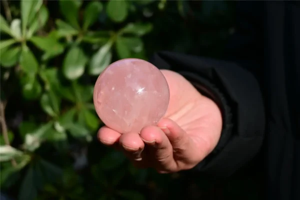 May include: A smooth, polished rose quartz sphere with a translucent, pale pink appearance. The crystal ball features natural internal inclusions and a reflect May include: A smooth, polished rose quartz sphere with a translucent, pale pink appearance. The crystal ball features natural internal inclusions and a reflective surface that catches the light, showcasing a soft, rounded shape and consistent color.