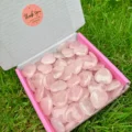 May include: A box filled with polished rose quartz heart-shaped stones. The box has a pink interior and a white exterior. A round sticker with the words "Thank You For Your Order" is on the box. The stones are a soft pink color.