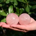 May include: Two smooth, polished rose quartz spheres with a translucent, pale pink hue. The stones exhibit natural internal fractures and cloudy inclusions throughout their rounded surfaces, showcasing the characteristic soft pink color of the mineral.