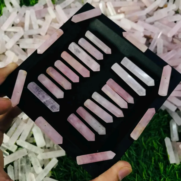 May include: A black velvet box filled with twenty pink crystal wands. The wands are arranged in rows and are all the same size. The box is surrounded by a pile May include: A black velvet box filled with twenty pink crystal wands. The wands are arranged in rows and are all the same size. The box is surrounded by a pile of smaller pink crystals.
