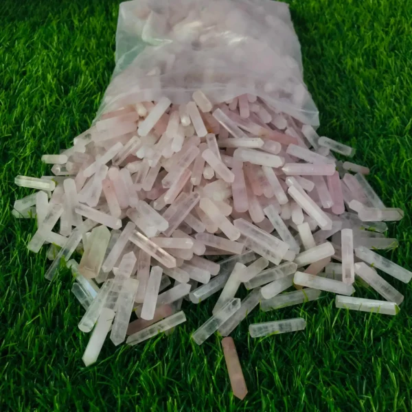 May include: A plastic bag filled with many small, pink and white crystal points. The points are arranged in a random pattern and are spilling out of the bag on May include: A plastic bag filled with many small, pink and white crystal points. The points are arranged in a random pattern and are spilling out of the bag onto a green surface.