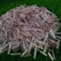 May include: A large pile of pink and clear crystal points, also known as wands, on a green grassy surface.