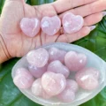 May include: A collection of pink rose quartz heart shaped crystals in a white bowl. The crystals are smooth and polished.