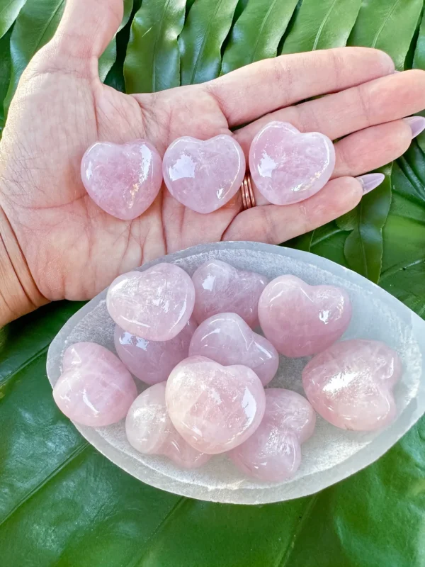 May include: A collection of pink rose quartz heart shaped crystals in a white bowl. The crystals are smooth and polished. May include: A collection of pink rose quartz heart shaped crystals in a white bowl. The crystals are smooth and polished.
