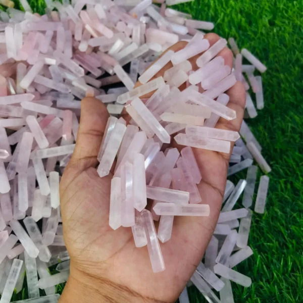 May include: A large pile of pink rose quartz points, some of which are being held in a hand. The points are various sizes and shapes. May include: A large pile of pink rose quartz points, some of which are being held in a hand. The points are various sizes and shapes.