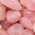 May include: A collection of smooth, pink rose quartz tumbled stones. The stones are various sizes and shapes, with a natural, polished finish.