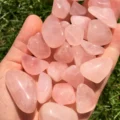 May include: A collection of tumbled rose quartz stones in various sizes and shapes. The stones are a pale pink color and have a smooth, polished finish.