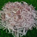 May include: A large pile of pink and clear crystal points, also known as wands, are arranged on a bed of green grass. The points are various sizes and shapes, with some having a slight iridescent sheen.