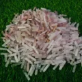 May include: A large pile of pink and white crystal points, also known as rose quartz points, are scattered on a green grassy surface.