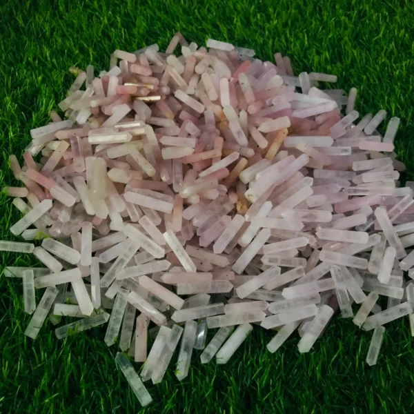 May include: A large pile of pink and white crystal points, also known as rose quartz points, are scattered on a green grassy surface. May include: A large pile of pink and white crystal points, also known as rose quartz points, are scattered on a green grassy surface.