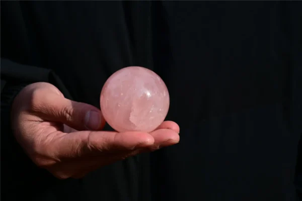 May include: A smooth, polished sphere made of translucent pale pink rose quartz. The stone features natural internal inclusions and a glossy surface that refle May include: A smooth, polished sphere made of translucent pale pink rose quartz. The stone features natural internal inclusions and a glossy surface that reflects light, showcasing a soft, uniform pastel pink color throughout the entire round object.