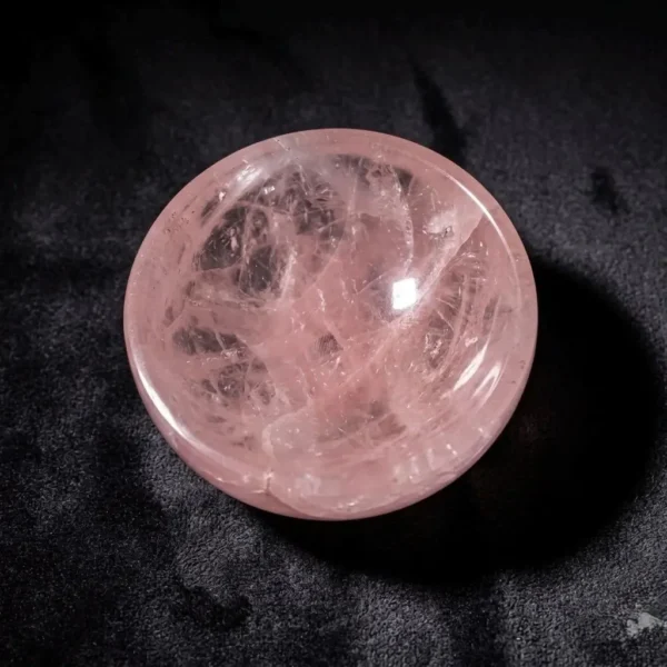 May include: A polished, round rose quartz bowl. The bowl is a soft pink color with internal veining and a smooth, reflective surface. The bowl is set against a May include: A polished, round rose quartz bowl. The bowl is a soft pink color with internal veining and a smooth, reflective surface. The bowl is set against a dark background.