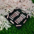 May include: A black tray filled with 20 pink rose quartz points. The points are arranged in rows and are all approximately the same size. The tray is sitting on a bed of green grass.