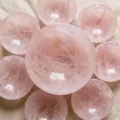 May include: A collection of rose quartz spheres in varying sizes, arranged in a circular pattern. The spheres are a soft pink color with internal veining, reflecting light. The arrangement includes a large central sphere surrounded by smaller ones.