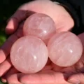 May include: Three polished rose quartz spheres with a translucent, pale pink appearance. Each stone features natural internal veining and a smooth, rounded surface, showcasing the characteristic soft pink hue and crystalline texture of the mineral.