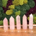 May include: Five light pink rose quartz crystal points arranged in a row on a wooden surface. Each point is numbered 6 through 10 at the base, showing a faceted top and a smooth, translucent body with natural internal inclusions and variations.