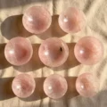 May include: Nine polished rose quartz spheres, each with a translucent pink hue, are arranged on a beige fabric. The spheres vary slightly in color and internal patterns, with shadows cast by the sunlight.