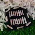 May include: A collection of 20 pink crystal wands displayed on a black tray. The wands are arranged in two rows of ten, with the points facing outward. The tray is surrounded by a scattering of smaller pink crystals.