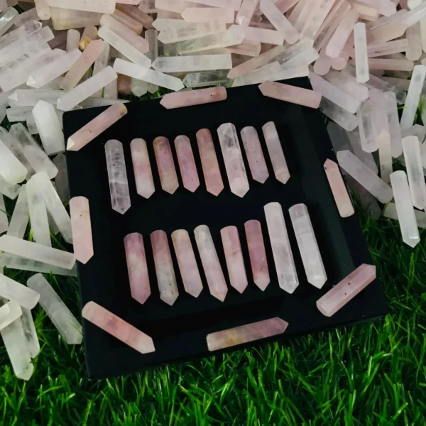 May include: A collection of 20 pink crystal wands displayed on a black tray. The wands are arranged in two rows of ten, with the points facing outward. The tra May include: A collection of 20 pink crystal wands displayed on a black tray. The wands are arranged in two rows of ten, with the points facing outward. The tray is surrounded by a scattering of smaller pink crystals.