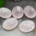 May include: Five smooth, oval-shaped rose quartz stones, polished to a high shine. The stones are pale pink and translucent, with a slight shimmer.