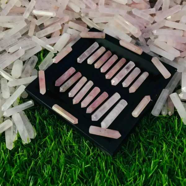 May include: A collection of 24 pink rose quartz crystal points arranged in rows on a black tray. The points are all approximately the same size and shape, and May include: A collection of 24 pink rose quartz crystal points arranged in rows on a black tray. The points are all approximately the same size and shape, and they have a natural, unpolished finish.