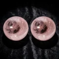 May include: Two polished rose quartz spheres. The spheres are a soft pink color with internal veining and a smooth, reflective surface. The spheres are displayed on a dark, textured background.