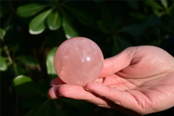 May include: A polished, spherical rose quartz crystal with a translucent, pale pink hue. The stone features natural internal inclusions and a smooth, reflectiv May include: A polished, spherical rose quartz crystal with a translucent, pale pink hue. The stone features natural internal inclusions and a smooth, reflective surface that catches the light, showcasing its soft, semi-opaque, and crystalline texture.